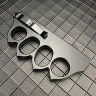 The back side of a closed black 1918 U.S. knuckle duster OTF knife, showing the silver pocket clip and four finger holes on a dark grid background.