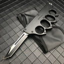 An open black 1918 U.S. knuckle duster OTF knife resting on its black nylon sheath, displayed on a dark grid background.