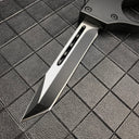A close-up of the silver tanto blade of a 1918 U.S. OTF knife, showing the central groove and sharp tip on a dark grid background.