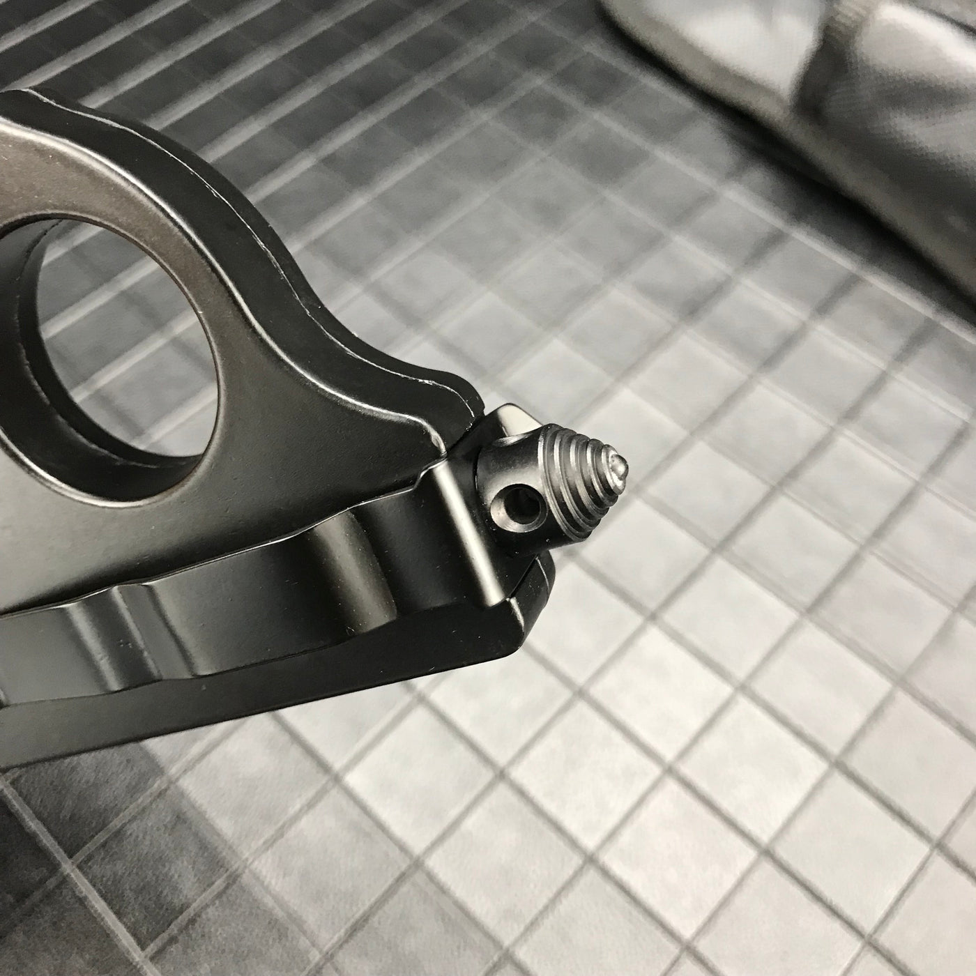A close-up of the threaded glass breaker tip on the handle of a black 1918 U.S. knuckle duster OTF knife, displayed on a dark grid background.