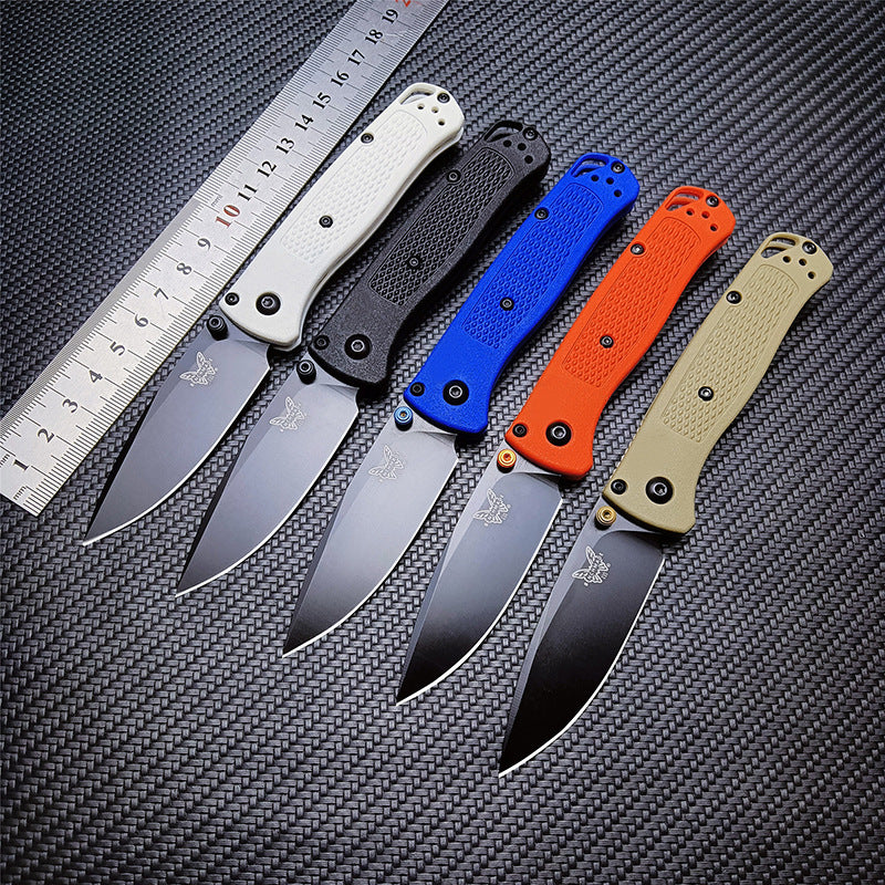 Five Benchmade folding knives in different colors placed next to a metal ruler on a dark textured surface for size comparison.