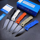 Five Benchmade folding knives in black, white, blue, orange, and tan, displayed with their blue box, warranty card, and sticker on a dark textured surface.