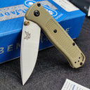 An open Benchmade folding knife with a tan handle, silver blade, and tan thumb stud, displayed with its blue box.