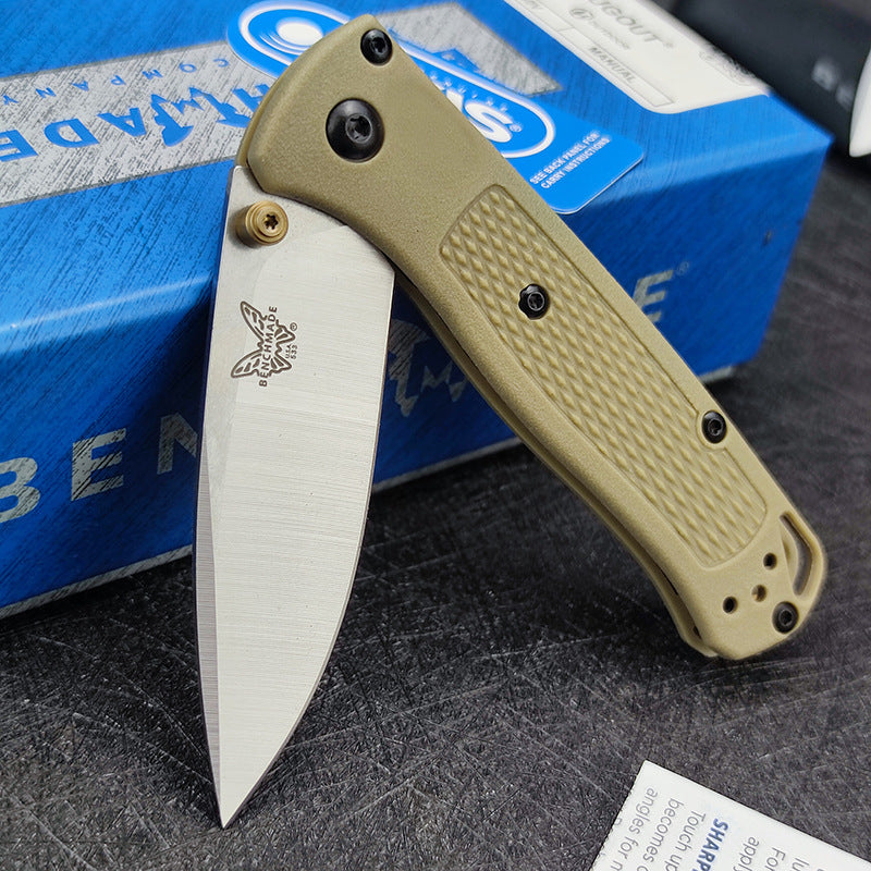 An open Benchmade folding knife with a tan handle, silver blade, and tan thumb stud, displayed with its blue box.