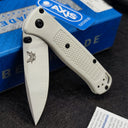 An open Benchmade folding knife with a white handle and silver blade, displayed with its blue box and a sticker.