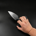 A hand holding an open black folding knife with a textured handle and a stonewashed blade in a tactical grip, displayed against a dark background.