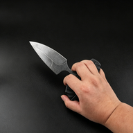 A hand holding an open black folding knife with a textured handle and a stonewashed blade in a tactical grip, displayed against a dark background.