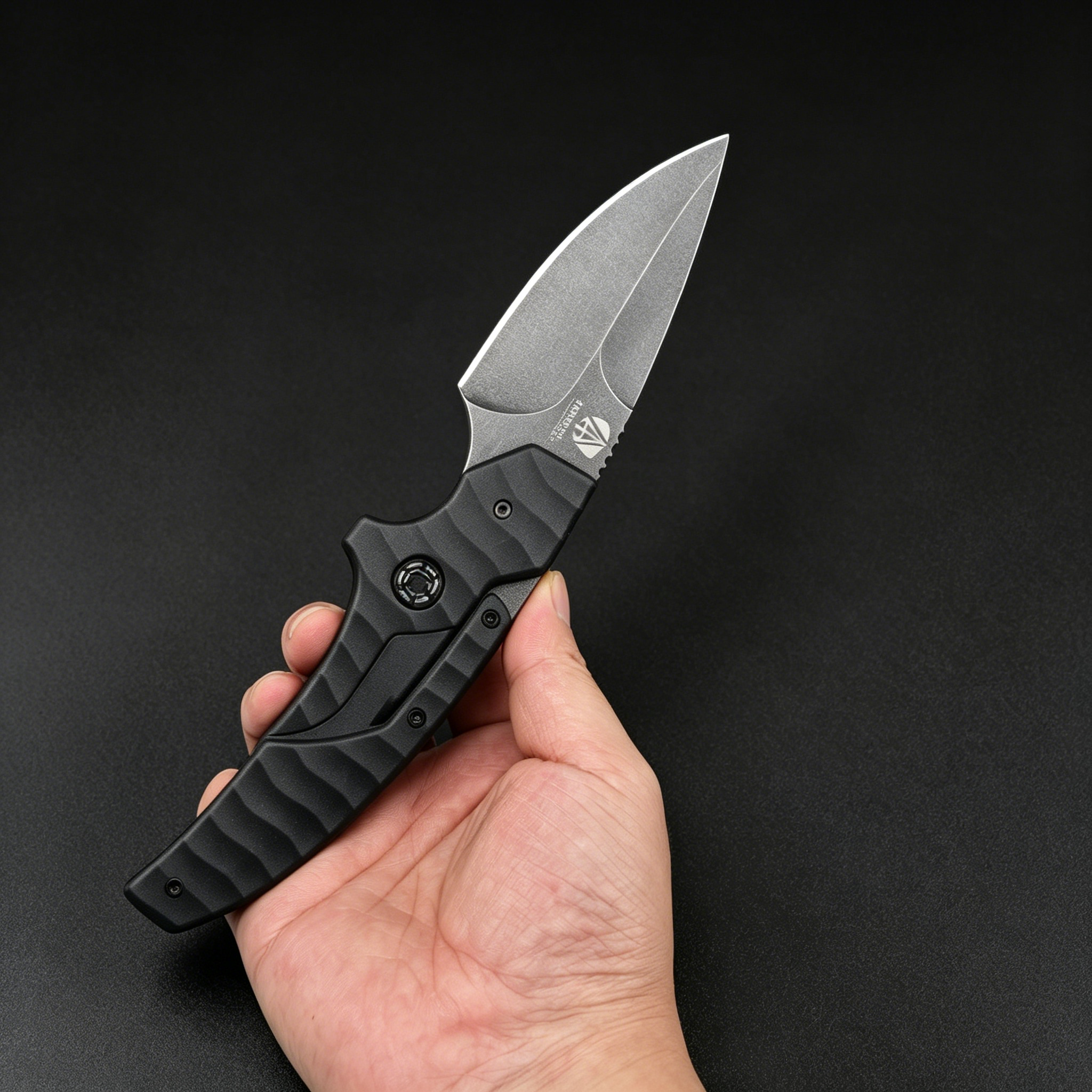 A hand holding an open black tactical folding knife with a textured handle and a silver stonewashed blade, displayed against a dark background.