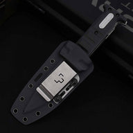 A sheathed folding knife with a black textured handle and silver hardware, resting inside a black hard plastic sheath equipped with a silver metal belt clip featuring a stylized logo, displayed on a dark background.