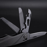 A close-up view of a black folding multi-tool with several attachments deployed, including a serrated saw blade, a grooved file, a bottle opener with wire stripper notches, and a smooth scraping blade.