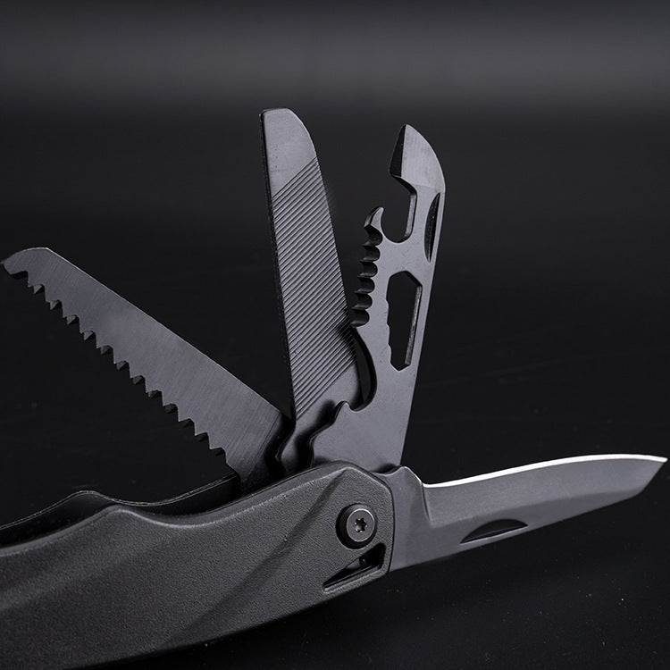 A close-up view of a black folding multi-tool with several attachments deployed, including a serrated saw blade, a grooved file, a bottle opener with wire stripper notches, and a smooth scraping blade.