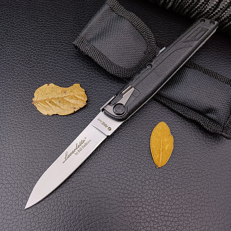 An open black-handled folding knife displayed next to its black nylon sheath and yellow leaves, featuring a textured grip.