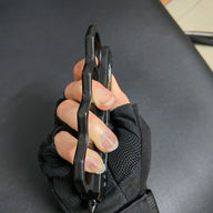 An edge profile view of a closed black knuckle duster OTF knife held by a hand, showing the thickness and the curved cutouts of the handle.