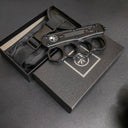 A closed black knuckle duster OTF knife resting on its packaging box and black nylon sheath, displayed on a dark surface.