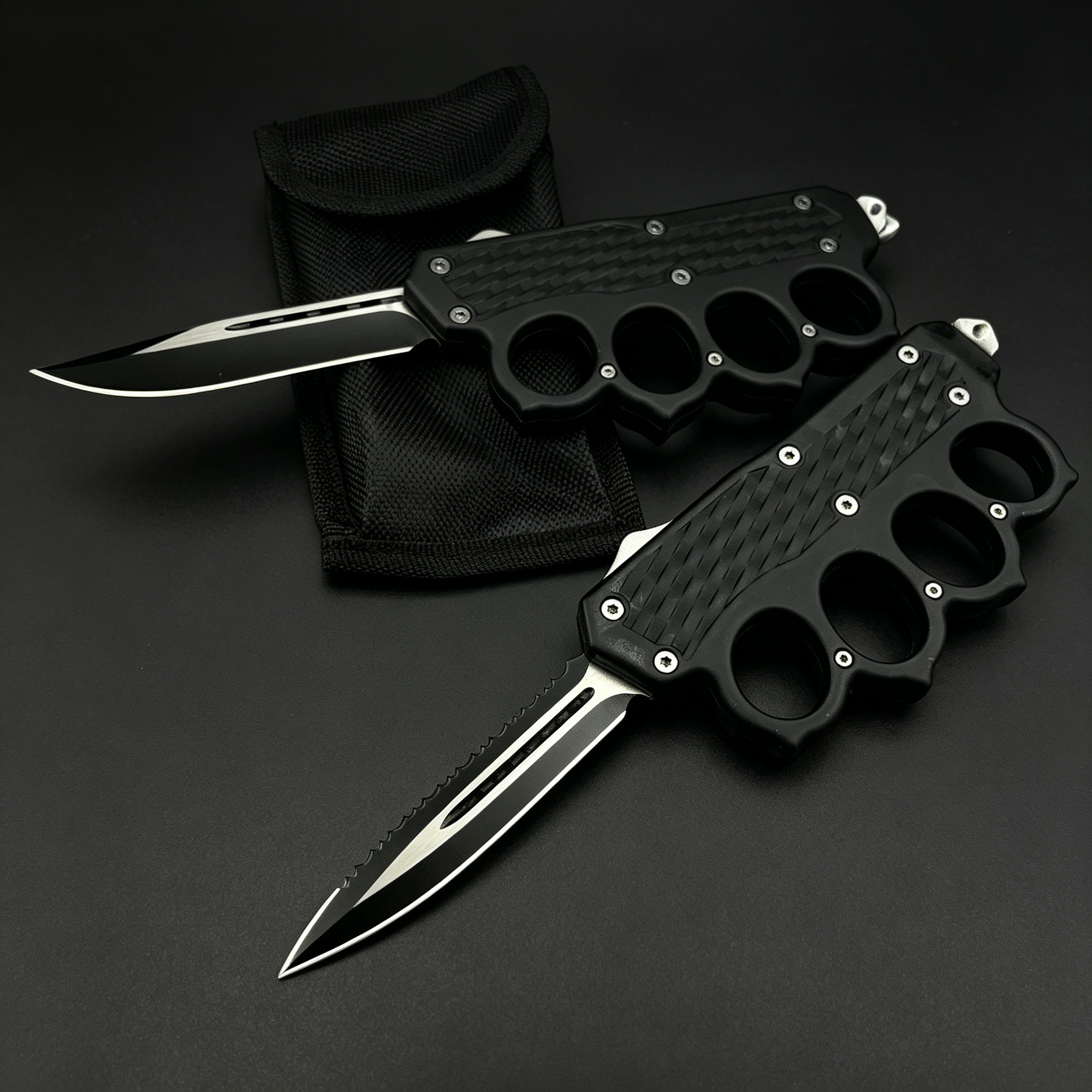 Two open black OTF knives with knuckle duster handles, one with a plain edge and one with a serrated edge, displayed on a black nylon sheath against a dark background.