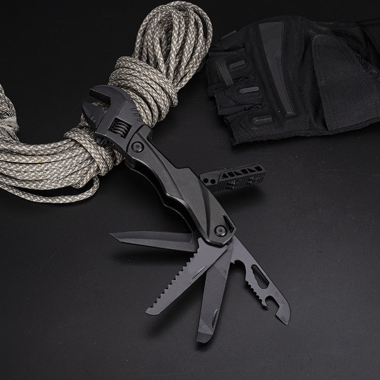 A black folding adjustable wrench multi-tool with multiple blades and tools deployed, displayed on a dark surface next to a coil of paracord and a black nylon sheath.