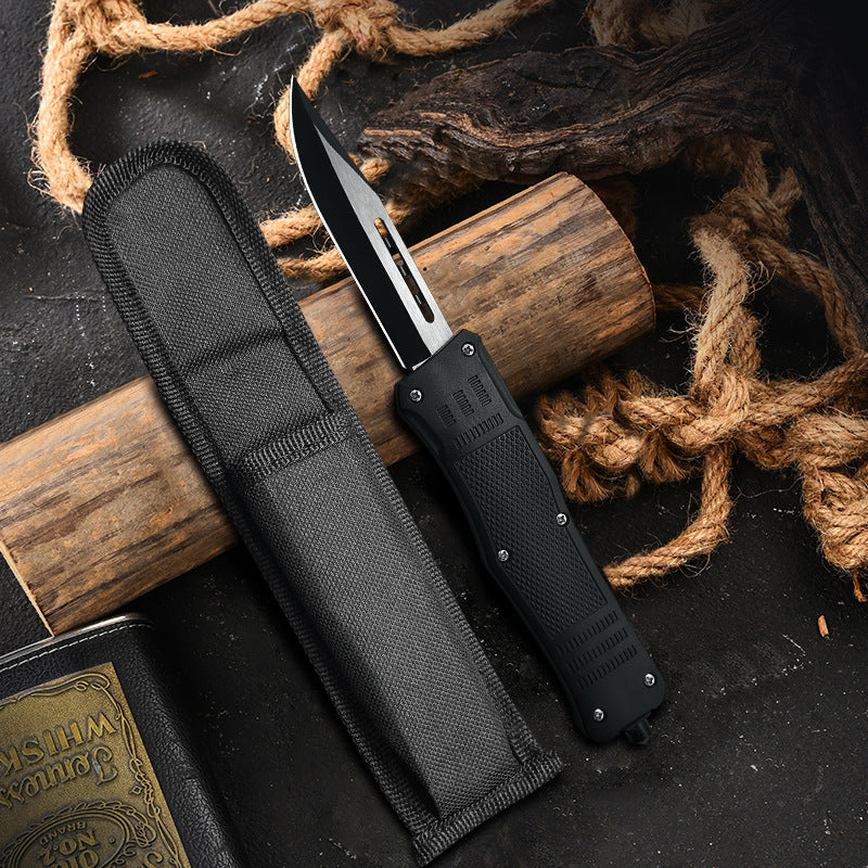 A black OTF knife with a textured handle and silver blade, displayed next to a black nylon sheath against a rustic background of wood and rope.