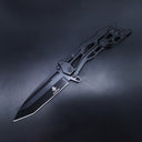 An open all-black tactical folding knife featuring a Tanto blade and a skeletonized handle, displayed on a dark background.