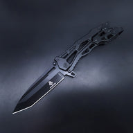 An open all-black tactical folding knife featuring a Tanto blade and a skeletonized handle, displayed on a dark background.