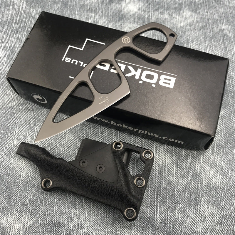 A Böker Plus skeletonized fixed blade knife displayed over its black packaging box and leather sheath on a denim-textured surface.