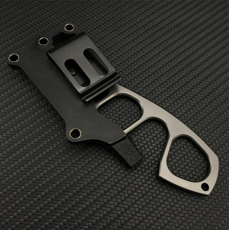 The back side of a black sheath for a Böker Plus neck knife, showing the polymer belt clip or mounting attachment, with the knife partially inserted, on a carbon fiber background.