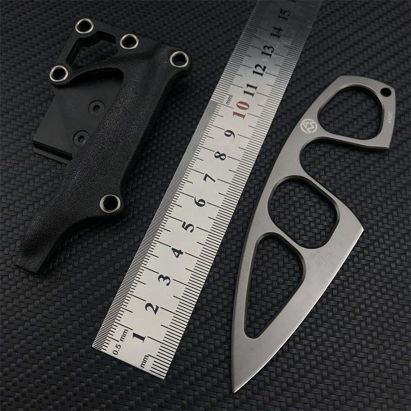 A Böker Plus skeletonized neck knife with its black leather sheath displayed next to a metal ruler on a carbon fiber textured background for size reference.