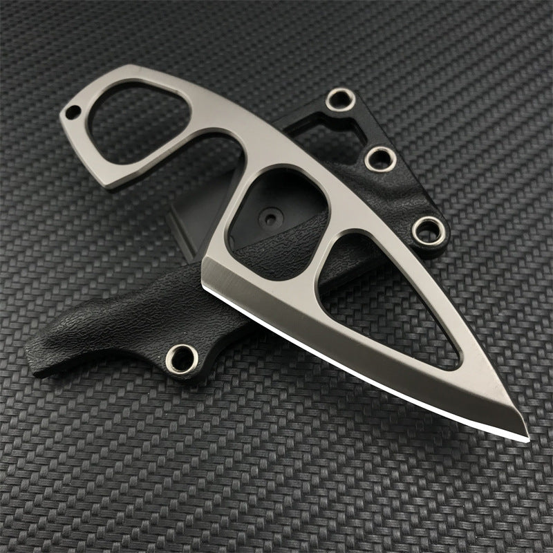 A Böker Plus 440C stainless steel neck knife with a finger ring, resting on its black leather sheath against a dark carbon fiber patterned background.