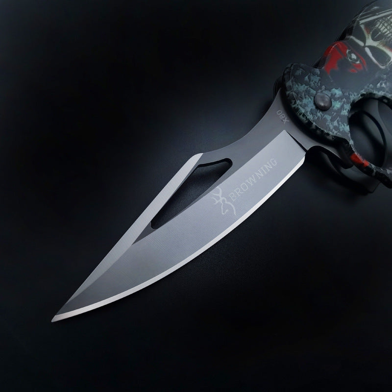 Close-up of the silver blade on a BROWNING knuckle duster folding knife, showing the angled cutout and logo engraving, against a dark background.