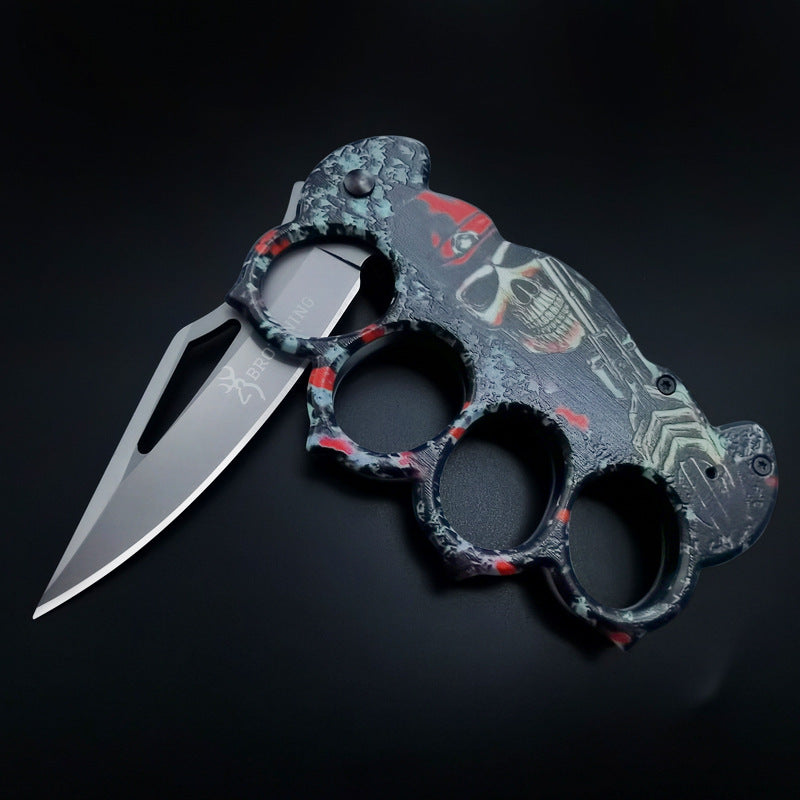 An angled view of an open BROWNING knuckle duster folding knife, highlighting the intricate skull and red details on the handle and the blade cutout design.