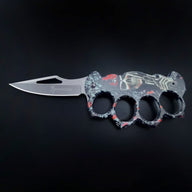 An open folding knuckle duster knife with a grey, red, and black skull and pistol graphic handle, featuring a silver blade with a cutout and the BROWNING logo, on a black background.