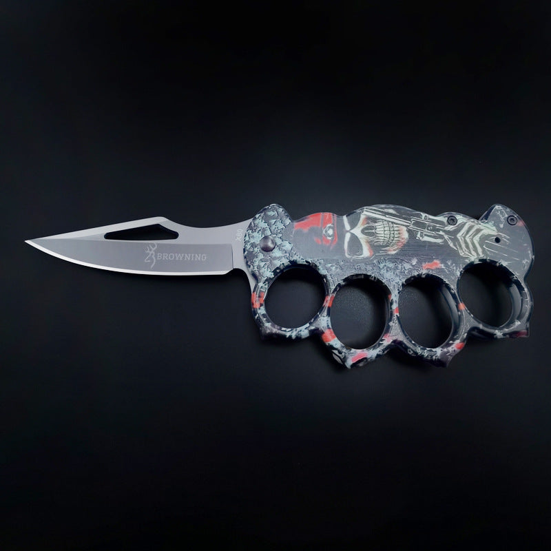 An open folding knuckle duster knife with a grey, red, and black skull and pistol graphic handle, featuring a silver blade with a cutout and the BROWNING logo, on a black background.
