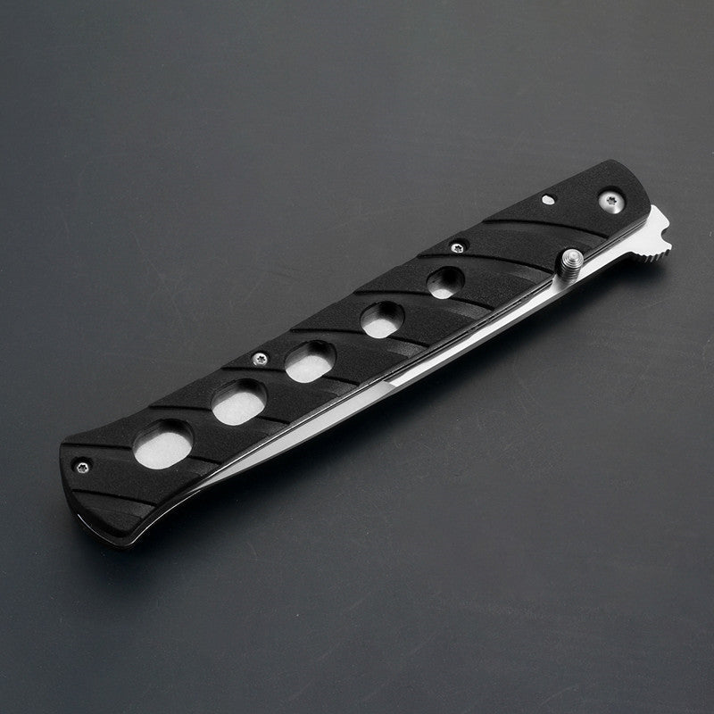A closed black folding knife featuring a handle with circular cutouts, a silver thumb stud, and a silver blade edge visible along the bottom, displayed on a dark gray background.