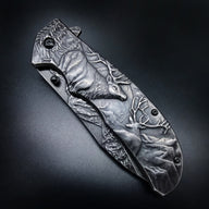A closed folding knife with deep relief engraving of several deer and forest scenery on the handle and blade, displayed on a dark textured background.