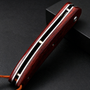 A closed folding knife with a polished red wooden handle and silver liners, featuring a brown lanyard at the end, resting against a black box on a dark textured background.