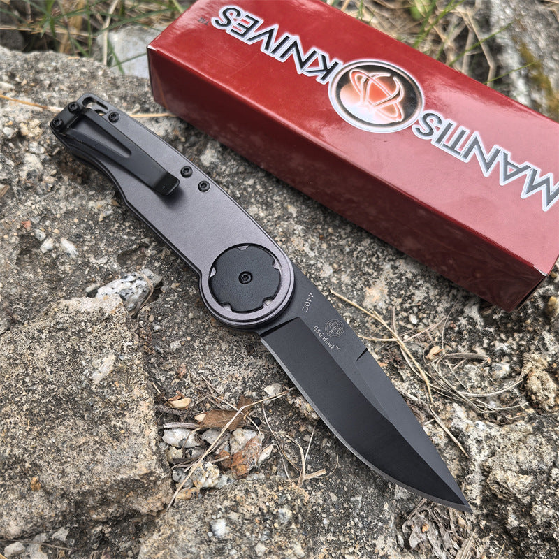 A closed folding knife with a grey handle and black pocket clip, resting on a red packaging box outdoors.