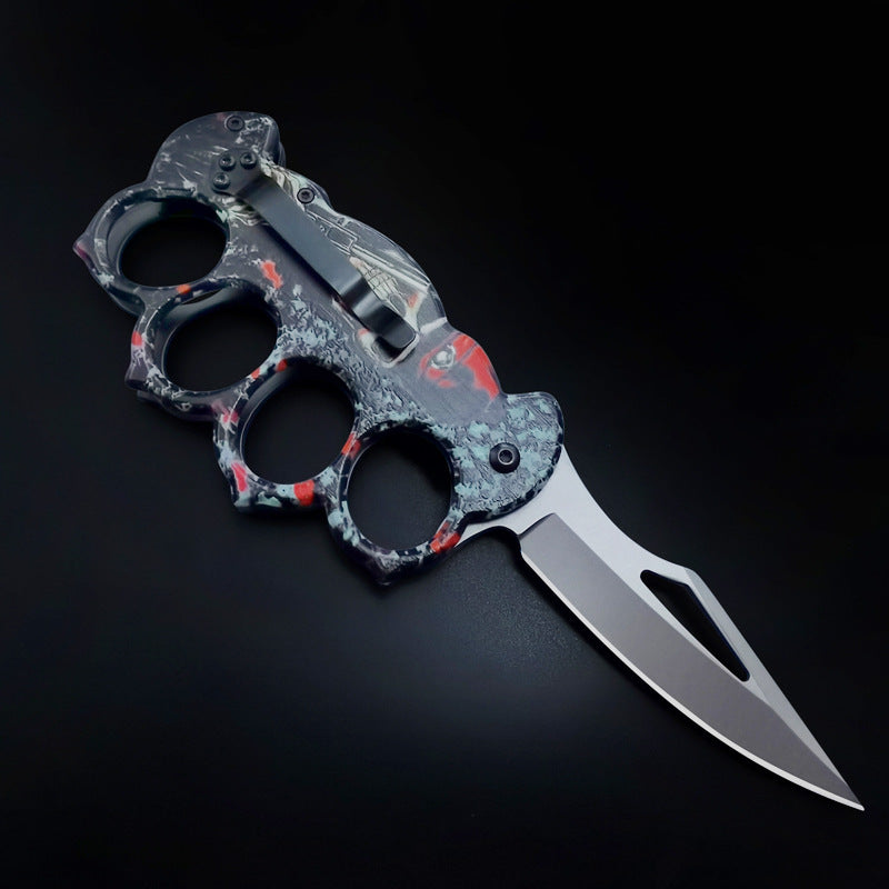 Side profile of a closed knuckle duster folding knife, showcasing the textured handle, pocket clip, and graphic design, on a dark background.