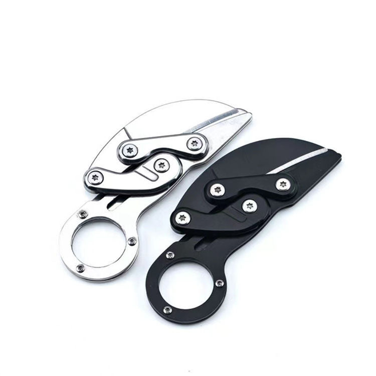 Two closed mechanical folding karambit knives with finger ring handles and visible star screws, one silver and one black, displayed on a white background.