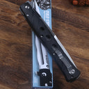 An open Cold Steel Ti-Lite folding knife with a black handle and silver pocket clip, resting on top of its blue packaging box on a wooden desk surface.