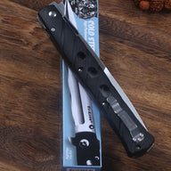 An open Cold Steel Ti-Lite folding knife with a black handle and silver pocket clip, resting on top of its blue packaging box on a wooden desk surface.