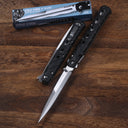 An open and a closed Cold Steel Ti-Lite folding knife with black handles and silver blades, displayed next to their blue packaging box on a wooden desk.