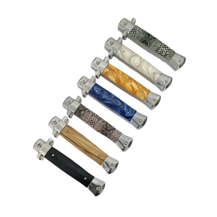  A collection of closed stiletto-style folding knives with various handle patterns including wood, black, blue resin, orange resin, white pearl, and snakeskin textures.