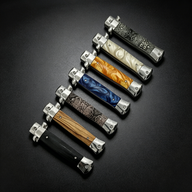  A collection of closed stiletto-style folding knives with various handle patterns including wood, black, blue resin, orange resin, white pearl, and snakeskin textures.