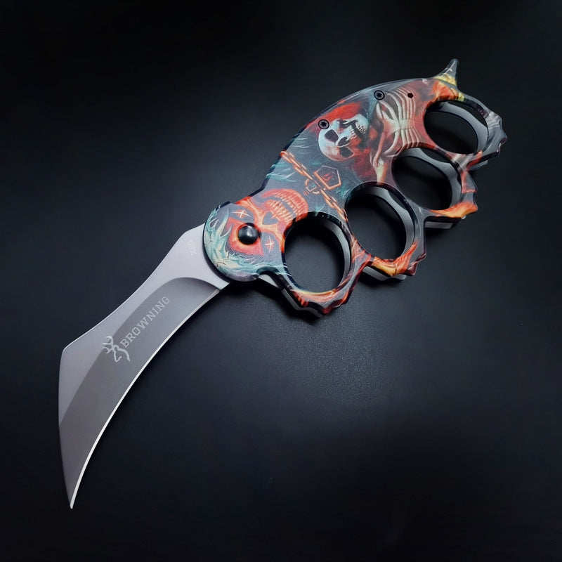 An open knuckle duster folding knife with a colorful skull graphic handle and a silver blade engraved with the BROWNING logo, displayed on a dark background.