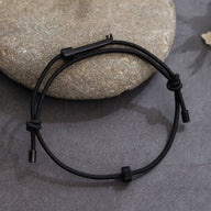 A black wearable tactical handcuff key displayed on a natural stone surface, highlighting its discreet and durable design for everyday carry.