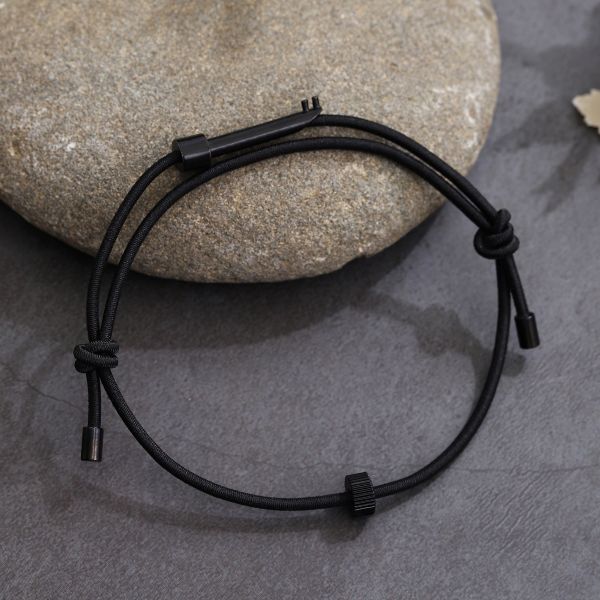 A black wearable tactical handcuff key displayed on a natural stone surface, highlighting its discreet and durable design for everyday carry.