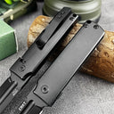 A close-up of two open CRKT folding knives showing the black handles and pocket clips, resting next to a wood log on a grey surface.