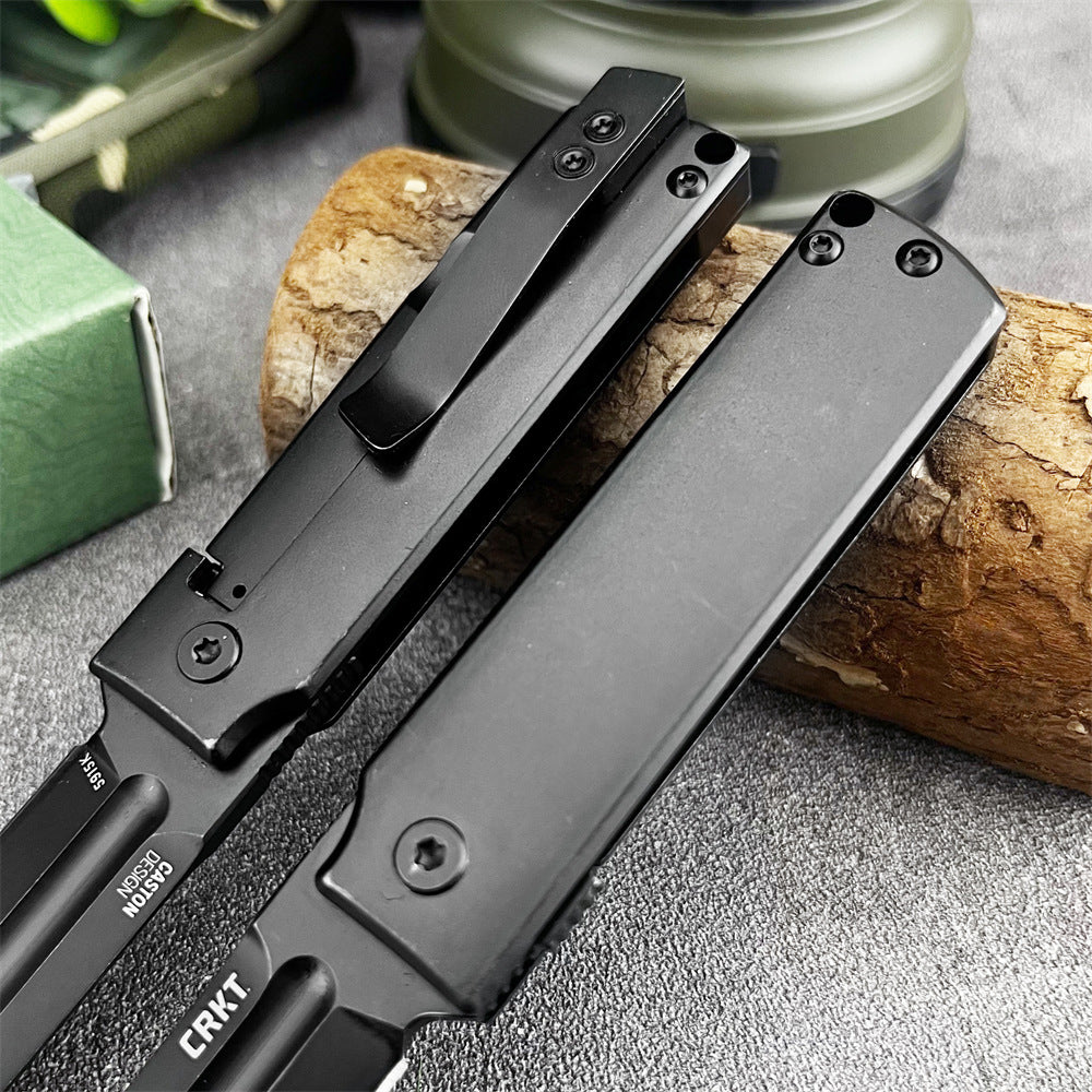 A close-up of two open CRKT folding knives showing the black handles and pocket clips, resting next to a wood log on a grey surface.