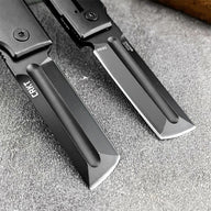 A close-up of two CRKT knife blades, one with a grey finish and one with a black finish, showing the steel markings and CRKT logo.