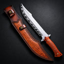 A custom fixed blade knife with a carved wooden handle and a silver blade with black flame patterns, displayed next to a brown leather sheath on a dark surface.