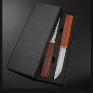 An open black gift box containing a set of D2 steel fixed blade knives with wooden handles and brass accents, displayed on a dark background.